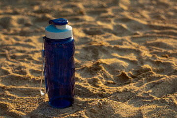 Blue plastic water bottle and sunglasses on the sand of a beach