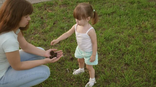 healthy baby and mom play and collect cones in the park. Mother shows her daughter pine cones. The concept of happy childhood. Happy family is walking with a child on the lawn.