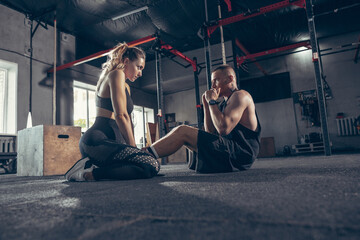 Fototapeta na wymiar Beautiful young sporty couple workout in gym together. Caucasian man training with female trainer. Concept of sport, activity, healthy lifestyle, strength and power. Working out ABS. Inclusion.