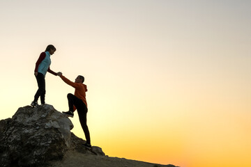 Man and woman hikers helping each other to climb a big stone at sunset in mountains. Couple...