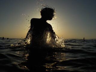 Silhouette of a child playing with the water in the sea 