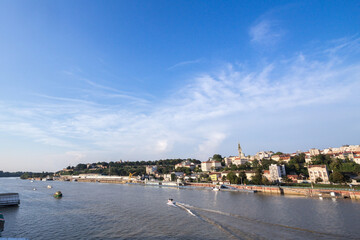 Fototapeta na wymiar View of Sava river bank in Belgrade, Serbia. An orthodox cathedral church can be seen on the right, Kalemegdan fortress on the background, and boats passing on the river