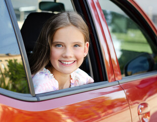 Happy cute little girl child looks out the window of the car