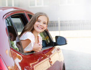 Happy cute little girl child looks out the window of the car