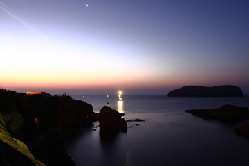 Fototapeta premium Ventotene, Italy - July 30, 2009: The sun rising at dawn on the island with boats in front of the island of Santo Stefano