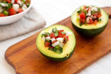 Homemade Pico de Gallo Stuffed Avocado on a rustic wooden board on a white wooden background, side view. Close-up.