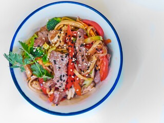 Udon noodles with meat in a plate on a white surface. With vegetables greens