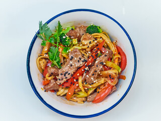 Udon noodles with meat in a plate on a white surface. With vegetables greens