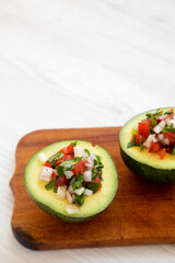 Homemade Pico de Gallo Stuffed Avocado on a rustic wooden board on a white wooden surface, side view. Space for text.