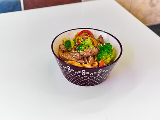 Udon noodles with meat in a plate on a white surface. With vegetables greens