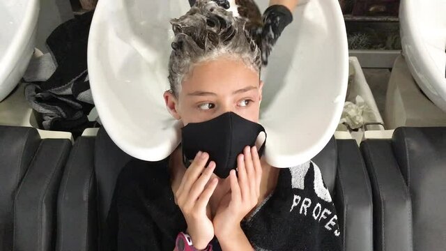 Young girl at the hairdresser's. Hairdresser's hands washing the hair of a girl wearing a face mask. Concept of new normality.