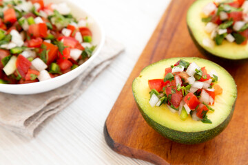 Homemade Pico de Gallo Stuffed Avocado on a rustic wooden board on a white wooden background, low angle view.