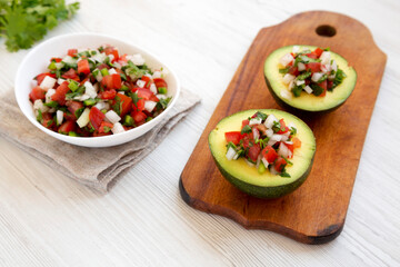 Homemade Pico de Gallo Stuffed Avocado on a rustic wooden board on a white wooden table, low angle view.