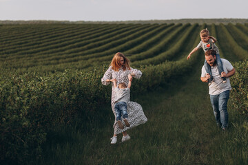 Big young happy family in the field on the nature. Mom, dad and 2 sons are having fun, running, fooling around together. Happiness and smiles around