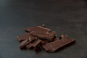 Dark chocolate stack, chips and cocoa powder on a dark background. Confectionery and food concept. Top view, copy space, selective focus..