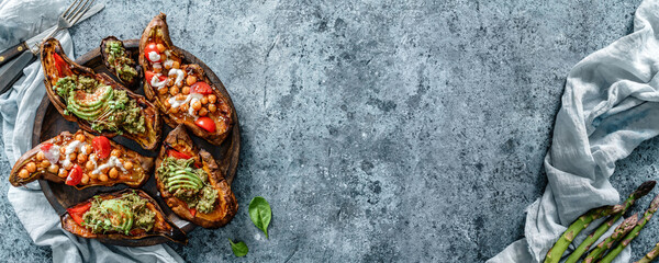 Obraz na płótnie Canvas Baked sweet potato toast with roasted chickpeas, tomatoes, goat cheese, sauce guacamole, avocado, seedlings on wooden board over blue background. Healthy vegan food, clean eating, dieting, top view