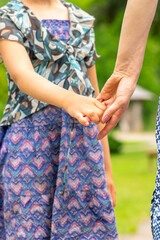 Mother and child concept. Young girl hold woman with a blue dress hand. Hands is in camera focus