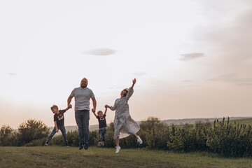 Big young happy family in the field on the nature. Mom, dad and 2 sons are having fun, running, fooling around together. Happiness and smiles around