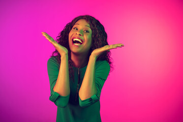 Surprising. African-american young woman's portrait on gradient pink background in neon light. Beautiful female model. Concept of human emotions, facial expression, sales, ad. Copyspace.