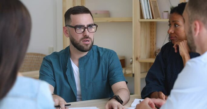 Serious male boss ceo executive talk to diverse people at group meeting seminar explain corporate strategy sit at table, focused workers group listen businessman team leader mentor teaching staff