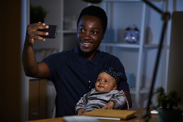 African happy father making selfie with his baby daughter on mobile phone while they sitting at the table