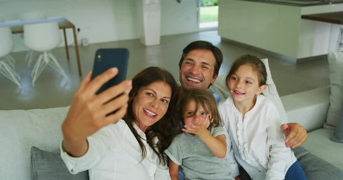 Authentic shot of happy smiling family are making a selfie or video call with a smartphone to friends or relatives on a sofa in a living room.