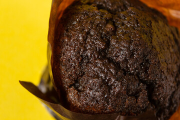 Chocolate muffin in paper on a yellow background