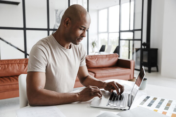 Photo of african american man working with laptop while sitting at table