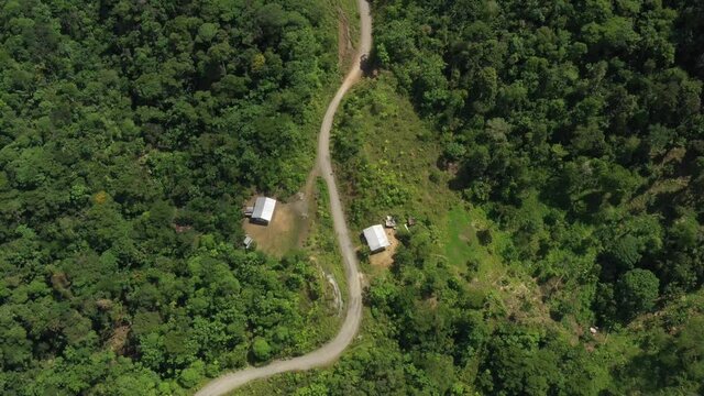 Two houses with tin roofs along a dirt road and surrounded by tropical forest
