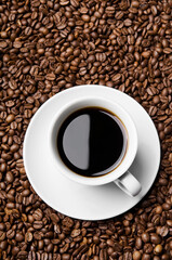 Cup of coffee drink sitting on a bed of roasted coffee beans background. Close up of a brown surface texture of aroma black caffeine drink ingredient for coffee beverage.