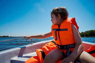 little girl in a swimming vest sits in a motorboat 