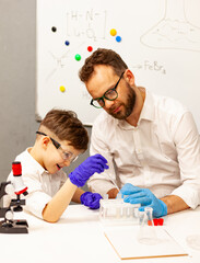 dad and son the child stayed at home conduct experiments on a white table, behind them on the wall is a white Board magnetic-marker