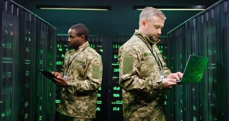 Mixed-races male military co-workers operating with data in server center and checking information...
