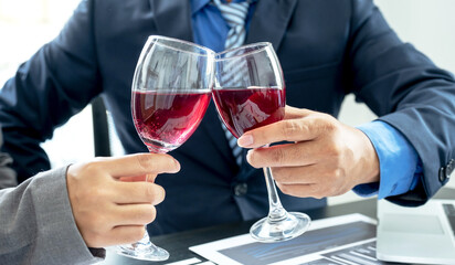 Two business executives people,.businesswomen, and businessman in a suit is bumping into a glass of wine celebrating success at the office desk. After the meeting