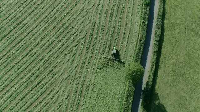 Aerial of a tractor tedding alongside a hedgerow and country rural road.