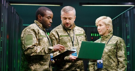 Male and female multiethnic army officers standing in monitoring analytic cener with servers with...