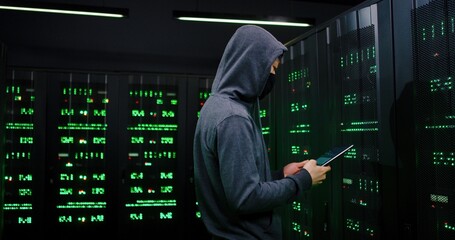 Asian male hacker hacking server system in dark sorage room with green lights. Police running in...