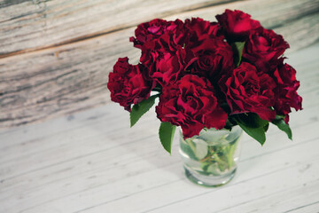 Dark red roses in vase on gray wood background with copy space.