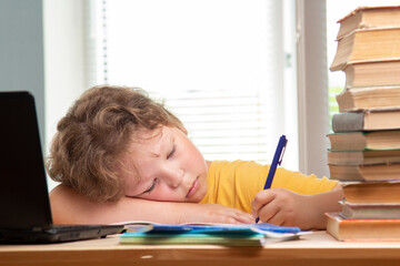 Tired schoolboy sitting at table doing homework.