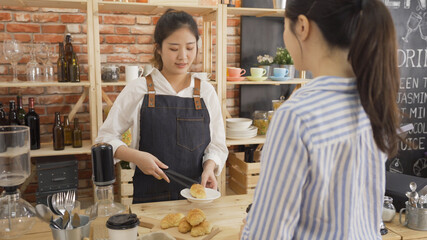 female waiter putting one of crusty croissants on plate for client of cafe bar. young business woman worker waiting for waitress prepare order in counter of coffee store. smiling good service concept