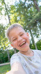 Authentic Funny small boy taking selfies and laughing. Smiling cute boy taking photos and facetime chatting with family. Vertical photo.