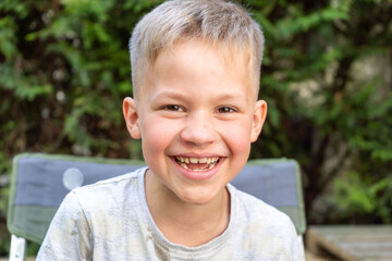 Cute boy portrait smiling and looking into Camera. Happy handsome child outdoors on a sunny day with toothy smile. 