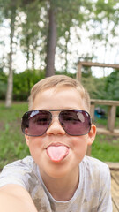 Funny small boy in glasses taking selfies and grimacing. Smiling cute boy taking photos and facetime chatting with family.