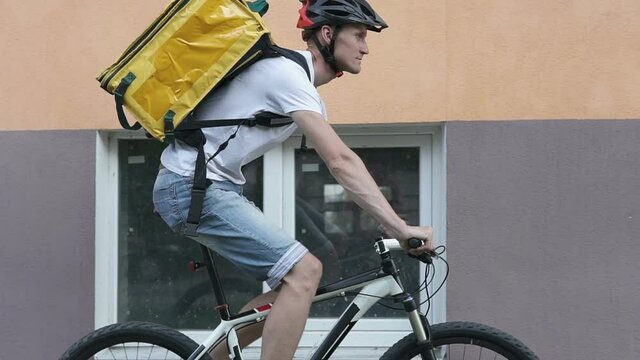 A courier in a protective helmet makes delivery of the order to customers by bicycle in the city center.