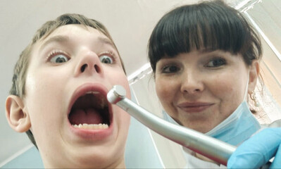 Scared boy at the dentist`s appointment. dentist doctor holds in his hands a machine for drilling...