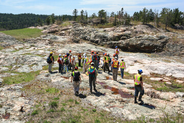 SUDBURY, ONTARIO, CANADA - MAY 21 2009: Group of workers and geologists in hardhats and high-visibility vests standing on geological outcrop site.