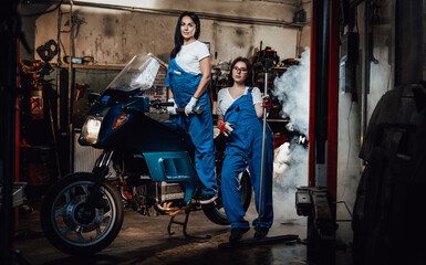 Fototapeta na wymiar Two young female mechanic posing next to a sportbike in authentic workshop garage