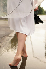 Fototapeta na wymiar a girl in a white dress with red hair with an umbrella walks through puddles after rain at sunset