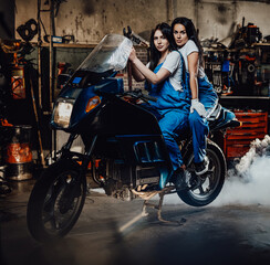 Two beautiful female mechanic sitting on sportbike in authentic workshop garage