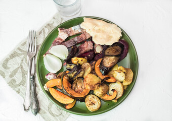 Baked vegetables on a plate, next to herring and unleavened bread